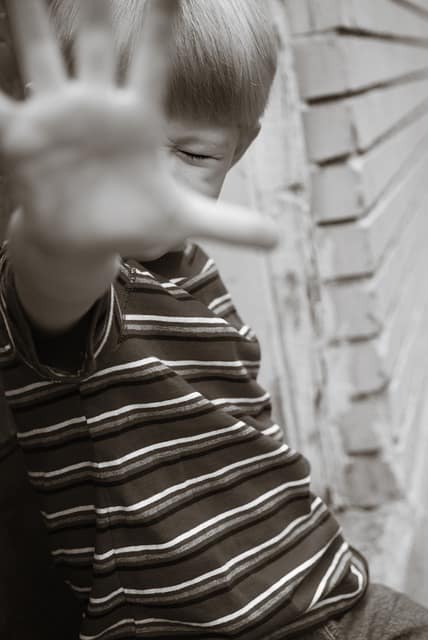 Close up of a young boy with his eyes closed and his hand up towards the camera in a stop gesture.