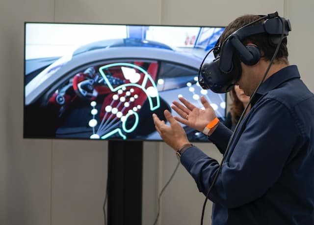 Man standing in front of TV screen with augmented reality glasses with ear phones.