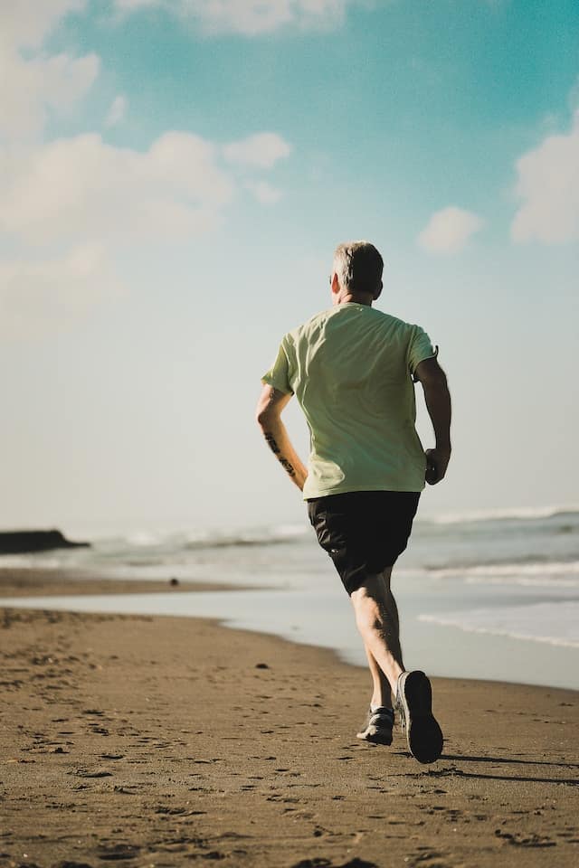 man on a beach running away from the camera along the shoreline.
