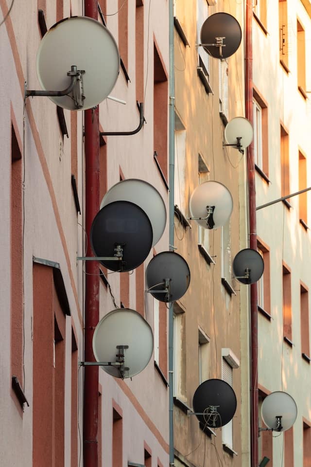 side of an apartment building with 11 satellite dishes mounted to the side of the building.