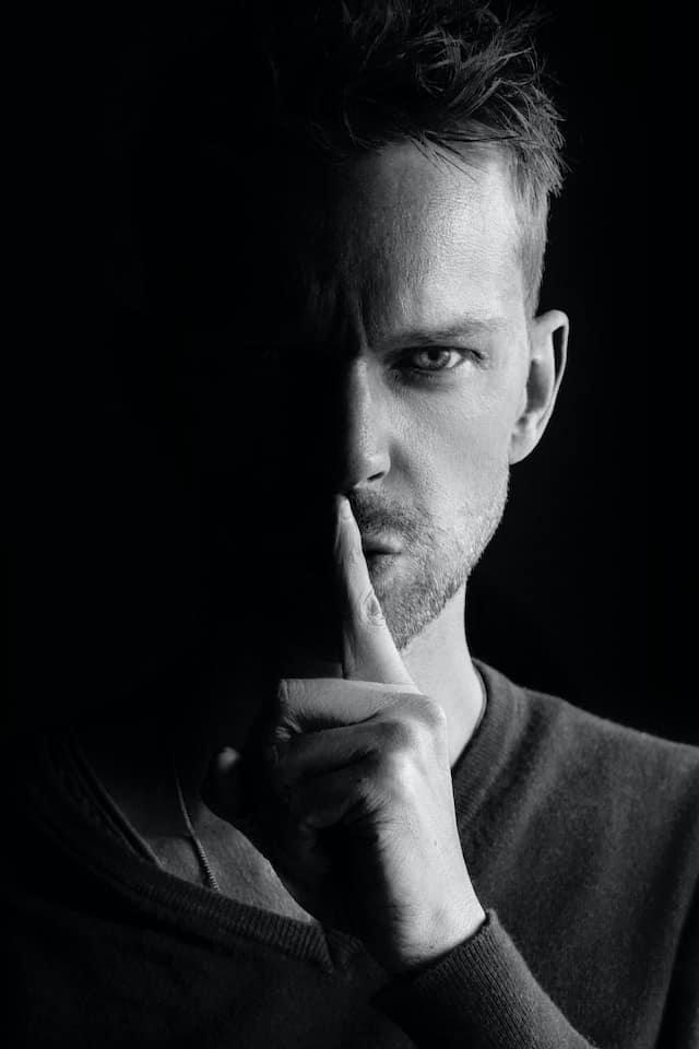 Black and white picture of a man with his finger to his mouth, shush up and keep quite.