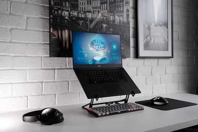 Laptop on a stand with a full-size keyboard on the table in front of it. The screen on the laptop shows a brain and futuristic image with AI imposed over the top.