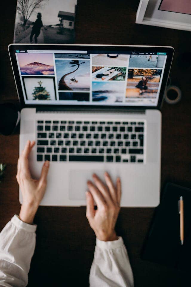 The is a a person's arms at a desk with a laptop which is on a page of images.